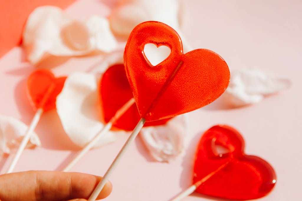 Red heart-shaped lollipops with white petals on a pink backdrop, perfect for romantic themes.